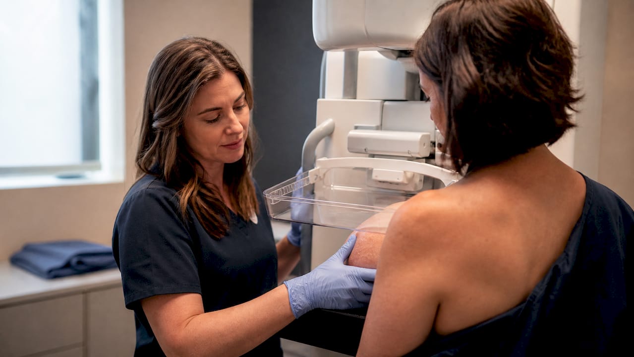Technologist positioning breast for mammogram screening